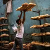 Un hombre levanta canastas con pan en un ambiente de panadería. Las paredes son azules y desgastadas.