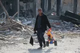 Un homme porte un seau et un jouet dans un paysage de débris.