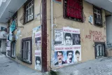 L'image montre un bâtiment dont la façade est recouverte de plusieurs affiches et de graffitis. Les affiches affichent des visages de personnes, probablement des portraits photographiques. Certains des textes sur les affiches et les murs semblent poser des questions, comme "Neredesin?" (Où es-tu ? en turc). L'ensemble donne une impression de revendication sociale ou politique, avec des références à un groupe. Les fenêtres sont protégées par des barreaux, ce qui ajoute une touche d'urbanité à la scène. La photographie semble capturer un moment dans un environnement urbain, peut-être dans une ville en Turquie.