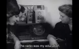 L'immagine mostra due donne sedute vicino a un vecchio radio. Sul tavolo accanto a loro ci sono delle fotografie incorniciate, tra cui una bandiera degli Stati Uniti. Sottili raggi di luce si riflettono sugli oggetti, creando un'atmosfera nostalgica. Una delle donne sembra riflettere sul passato, mentre una didascalia sottolinea l'importanza della radio come fonte di istruzione nella loro vita.