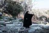 Femme en habit noir dans un cimetière, entourée de pierres tombales et de débris.