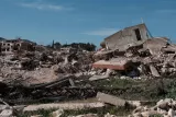 Ruines de bâtiments effondrés, débris et végétation dans un paysage dévasté.