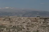 Terrains dévastés, bâtiments en ruines, montagnes en arrière-plan. Atmosphère désolée.
