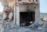 Des hommes assis devant un bâtiment partiellement détruit, entourés de débris.