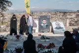 Des personnes en deuil dans un cimetière, avec des portraits et des bouquets de fleurs.