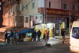 L'image montre une scène nocturne dans une rue urbaine. On peut voir des bâtiments avec des façades lumineuses, ainsi qu'une échoppe de restauration rapide appelée "Efeteya Pasta & Tava". Plusieurs personnes marchent dans la rue, certaines portant des vêtements décontractés et des couvertures sur la tête, ce qui crée une atmosphère animée. On remarque également des lampadaires éclairant la scène, ajoutant une ambiance nocturne.