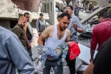 Une personne porte un enfant au milieu d'un bâtiment effondré et de débris.