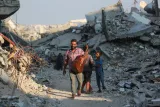Homme avec une guitare marche entre des décombres, suivi d'un enfant.
