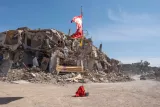 Un drapeau flotte devant un bâtiment effondré, sur un sol poussiéreux.