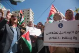 L'image montre un groupe de femmes participant à une manifestation. Elles tiennent des pancartes avec des slogans et des drapeaux palestiniens. Les expressions sur leurs visages suggèrent une forte détermination et un engagement pour leur cause. En arrière-plan, on aperçoit des bâtiments et un ciel bleu. L'ambiance est à la fois dynamique et solennelle, reflétant la passion des manifestants pour leurs droits et leur identité.
