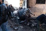 L'image montre un groupe de personnes rassemblées dans une rue dévastée. Le sol est jonché de débris, et l'ambiance semble chaotique. Au centre, un homme semble essayer de déplacer un grand objet, probablement un débris ou un meuble, tandis que d'autres observateurs se tiennent autour, certains se penchant pour examiner les alentours. Les bâtiments au fond sont en mauvais état, ce qui suggère qu'ils ont subi des dommages. L'éclairage est plutôt froid, ajoutant à l'atmosphère de désolation.