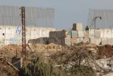 Zone de conflit avec un mur, des barbelés et un soldat en arrière-plan.