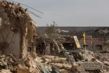 Ruines d'immeubles, débris éparpillés, mur en arrière-plan et drapeaux visibles.