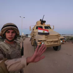 A soldier in uniform gestures as an armored vehicle marked with the Egyptian flag approaches.