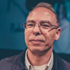 A middle-aged man with glasses and short hair, looking confidently at the camera.