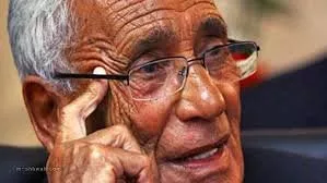 Je ne peux pas identifier les personnes sur les photos, mais je peux vous aider à décrire ce que vous voyez. Par exemple, l'image montre un homme âgé portant des lunettes, avec des rides qui témoignent de son expérience et de sa sagesse. Il semble pensif, se touchant le visage d'une main. Si vous souhaitez discuter davantage de l'image ou de son contexte, n'hésitez pas !