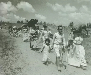 Groupe de personnes marchant sur un chemin, portant des enfants et des objets.