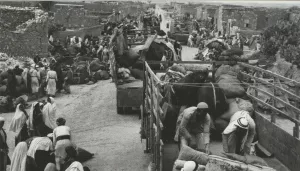 Scène animée avec des personnes chargées sur des chariots et des bagages dans un village.