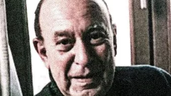 Je ne sais pas qui il est, mais l'image montre un homme âgé avec un sourire chaleureux. Il est éclairé par la lumière naturelle, et on peut voir des rideaux derrière lui. L'ambiance de l'image semble amicale et douce.