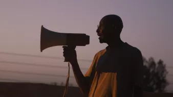 Un homme en silhouette tenant un mégaphone au crépuscule.