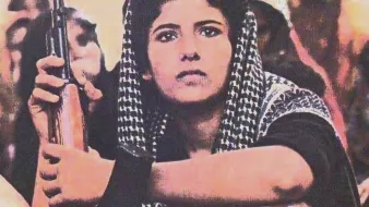 این تصویر نشان‌دهنده‌ی یک فرد جوان است که نشسته و یک تفنگ در دست دارد. او چهره‌ای محکم و متمرکز دارد و به دور و بر خود نگاه می‌کند. لباس‌های او به سبک سنتی و با فرهنگی خاص طراحی شده است. همچنین، این تصویر زمینه‌ای از فعالیت‌های اجتماعی یا سیاسی را ترسیم می‌کند و به نظر می‌رسد که نشان‌دهنده‌ی زمان و حوادث مهمی باشد.