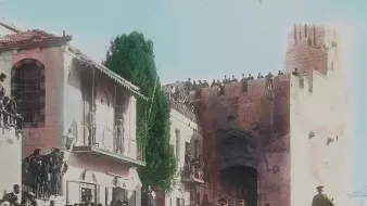 در این تصویر تاریخی، یک گروه از نظامیان در حال عبور از خیابانی در شهری با معماری قدیمی هستند. در دو طرف خیابان، جمعیتی زیادی ایستاده‌اند و به تماشای اتفاقات می‌پردازند. در پس‌زمینه، ساختمان‌هایی با طراحی خاص و دیواری بزرگ دیده می‌شوند. برخی از افراد در بالای دیوار ایستاده‌اند و نظاره‌گر هستند. فضای تصویر حسی از یک رویداد رسمی یا مراسم ویژه را القا می‌کند و رنگ‌آمیزی تصویر به آن جذابیت بیشتری بخشیده است.