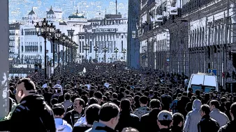 L'image montre une foule dense de personnes marchant dans une rue, probablement dans une ville animée. Les bâtiments sur les côtés semblent historiques, avec une architecture riche. On peut voir des lampadaires le long de la promenade, et au loin, on aperçoit des collines ou des montagnes qui ajoutent à la profondeur de la scène. L'atmosphère semble vibrante et dynamique, reflétant probablement une manifestation ou un événement public.