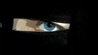 L'image montre un gros plan sur un œil visible à travers une pièce de tissu noir, probablement un voile. L'œil est d'une couleur claire, et le contraste avec le tissu sombre met en avant son expression. L'éclairage est subtil, ce qui ajoute une ambiance mystérieuse à l'image.