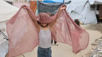 Bambino felice che salta con un velo rosato, in un ambiente di tende.