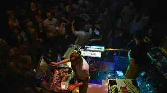A lively crowd enjoys live music from performers with electronic instruments on stage.