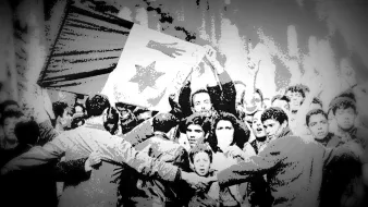 L'image montre une scène de rassemblement populaire où des manifestants brandissent une grande bannière ou un drapeau. Les participants semblent célébrer ou exprimer des revendications, et il y a une forte énergie collective. Certains visages sont visibles, reflétant diverses émotions, allant de la détermination à la joie. La composition en noir et blanc crée une atmosphère nostalgique et dramatique, soulignant l'importance historique de cet événement.