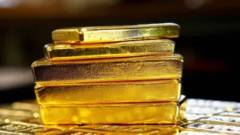 تظهر الصورة مجموعة من قضبان الذهب اللامعة، موضوعة بشكل متراص. القضبان ذات لون ذهبي براق، وتتميز بسطحها الأملس واللامع. يبدو أن القضبان ذات أحجام مختلفة، حيث تم ترتيبها بشكل عمودي، مما يبرز جمال الذهب وقيمته. يحيط بالصورة خلفية ضبابية وغير واضحة، ما يركز الانتباه على القضبان الذهبية.