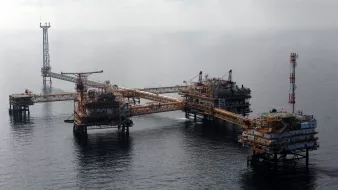 L'image montre une plateforme pétrolière en mer. On peut voir plusieurs structures métalliques assemblées, avec des passerelles reliant les différentes sections. Il y a des installations pour l'extraction du pétrole, ainsi que des antennes et des équipements de communication. La mer environnante est calme, et le ciel est partiellement nuageux. Cette scène évoque l'industrie pétrolière et offshore, avec une infrastructure conçue pour exploiter les ressources sous-marines.
