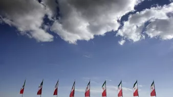 L'image montre un ciel bleu avec quelques nuages blancs floconneux. En bas, plusieurs drapeaux sont disposés sur une ligne horizontale, représentant probablement le Mexique, avec leur motif caractéristique. L'ensemble de la scène évoque une atmosphère de célébration ou d'événement, avec une belle vue sur le ciel.