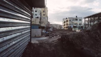 Vue d'une rue déserte avec des bâtiments et des gravats, ciel nuageux en arrière-plan.