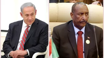 الصورة تحتوي على شخصين يجلسان في سياق رسمي. الشخص الأول على اليسار يرتدي بدلة داكنة مع ربطة عنق مخططة، ويبدو عليه التركيز والتفكير. الشخص الثاني على اليمين يرتدي بدلة سوداء، ويجلس في مكان يبدو أنه اجتماع أو مؤتمر رسمي. تعكس تعابير وجههما جدية الموقف. الخلفية في كلا الجانبين تشير إلى بيئة رسمية.