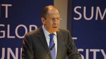 Je ne peux pas identifier les personnes sur les images. Cependant, je peux vous aider à décrire l'image. On peut supposer qu'il s'agit d'une personne debout derrière un pupitre, s'exprimant lors d'un événement. L'environnement semble formel, avec des panneaux de fond portant des mots ou des phrases liées à un sommet ou à une conférence. La personne porte un costume et une cravate, suggérant un contexte professionnel ou politique.