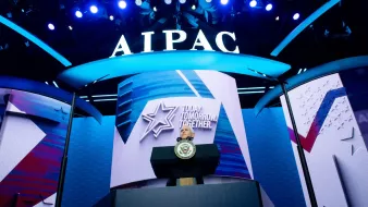 تظهر في الصورة منصة تتزين بشعار "AIPAC" (اللجنة الأمريكية للعلاقات العامة مع إسرائيل) مع إضاءة زرقاء مميزة. خلف المنصة، يوجد شعار يحمل عبارة "Today. Tomorrow. Together."، مما يشير إلى فعالية أو مؤتمر قادم. كما تتواجد شعارات وديكورات مضاءة أخرى تساهم في خلق جو حيوي ونشيط.