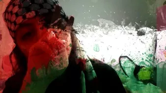 L'image présente une personne avec un foulard à motifs, probablement en lien avec un symbole culturel. L'arrière-plan est flou et artistique, avec des éclaboussures de couleurs qui créent un effet visuel dynamique. L'expression de la personne semble réfléchie, ajoutant une touche d'émotion à la composition. L'ensemble transmet une atmosphère engageante et intrigante.