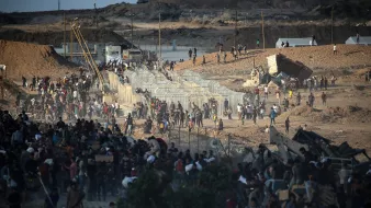 Une foule se rassemble près de clôtures dans un paysage aride et dévasté.