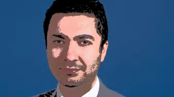 L'image présente un homme en costume, avec une chemise blanche et une cravate bleue. Il a les cheveux noirs et выглядит souriant. Le fond de l'image est bleu, ce qui contraste avec son costume plus sombre. Son expression semble confiante et professionnelle.