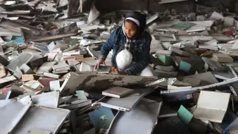 Una ragazza si trova in un luogo disordinato, circondata da libri e carte.