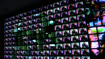 L'image présente une installation artistique composée de nombreux écrans alignés de manière à former un tableau visuel. Chaque écran affiche des images colorées, vibrantes et abstraites, créant un effet d'ensemble dynamique. Les couleurs se mélangent et se chevauchent, ajoutant une sensation de mouvement. La composition semble jouer avec la lumière et les contrastes, attirant l'œil vers des motifs diversifiés. L'ensemble évoque une immersion dans une expérience numérique moderne et artistique.