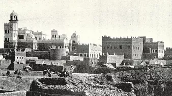این تصویر نشان‌دهنده‌ی یک منطقه تاریخی است که در آن ساختمان‌های قدیمی با معماری سنتی دیده می‌شوند. در پس‌زمینه، چندین ساختمان با سقف‌های گنبدی و تزئینات خاص وجود دارد. همچنین افرادی در حال کار در زمین‌های جلویی دیده می‌شوند که ممکن است مشغول کشاورزی یا ساخت‌وساز باشند. این صحنه، حال و هوای زندگی روزمره و تاریخی را در یک جامعه قدیمی به تصویر می‌کشد.
