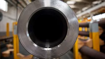L'image montre la vue de l'intérieur d'un grand tube métallique. On peut voir la texture lisse et brillante du métal au niveau de l'ouverture, tandis que l'intérieur du tube est sombre. En arrière-plan, des éléments d'un environnement industriel sont visibles, avec d'autres tubes et structures, suggérant un lieu de fabrication ou d'assemblage. L'éclairage est principalement naturel, créant un effet contrasté sur la surface du tube.
