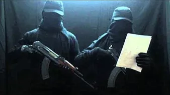 L'image montre deux individus habillés en noir, portant des masques et des casquettes. Ils tiennent des armes à feu, et l'un d'eux tient aussi un document. L'arrière-plan est sombre, ce qui accentue l'atmosphère mystérieuse de la scène.