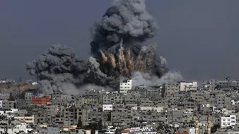 الصورة تظهر مشهدًا لمدينة تعرضت لتفجير، حيث تندلع سحب كثيفة من الدخان الأسود في السماء. يظهر تأثير الانفجار في المباني المحيطة، حيث تبرز آثار الدمار، بينما يبدو أن السماء ملبدة بالغيوم الناتجة عن الانفجار. المدينة تبدو كثيفة البنايات مع تشوهات واضحة نتيجة الأحداث المدمرة.