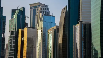الصورة تظهر مجموعة من ناطحات السحاب الحديثة في منطقة حضرية. تتميز المباني بتصاميمها المعمارية المتنوعة، حيث تختلف في الارتفاع والأشكال. الواجهة الزجاجية لبعض المباني تعكس الضوء مما يعطيها لمسة عصرية. الألوان تتراوح بين الزجاج الأزرق والأخضر، مع وجود لمسات من الذهبي والرمادي. السماء في الخلفية توحي بأوقات النهار، مما يضفي جواً حيوياً على المشهد.