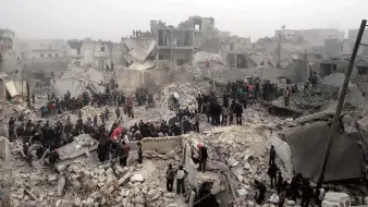 L'image montre un paysage de destruction massive, probablement après un événement catastrophique comme un tremblement de terre ou des bombardements. On aperçoit des bâtiments en ruines, réduits à des décombres, et une foule de personnes rassemblées sur les lieux. Elles semblent chercher des survivants ou explorer les débris. L'atmosphère est sombre et chaotique, reflétant une situation de crise et de désespoir.