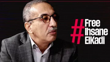 L'image montre un homme portant des lunettes et un costume à carreaux. Il semble participer à une interview ou à un débat, étant tourné vers un interlocuteur. À côté de lui, le texte en gras indique "#Free Ihsane ElKadi", suggérant qu'il est lié à une campagne de sensibilisation ou de soutien pour cette personne. L'arrière-plan présente un design graphique sobre, probablement pour mettre en avant le message.